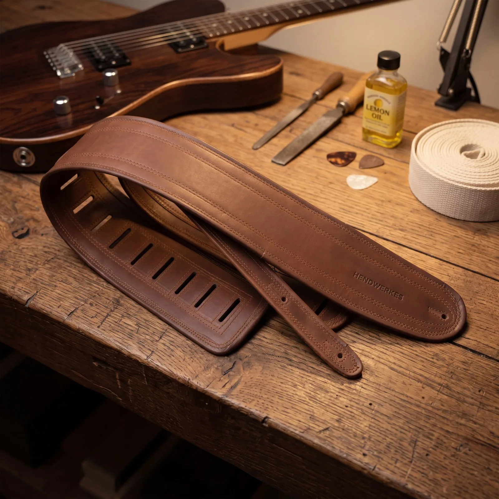 Heritage leather strap beside an electric guitar on a workbench